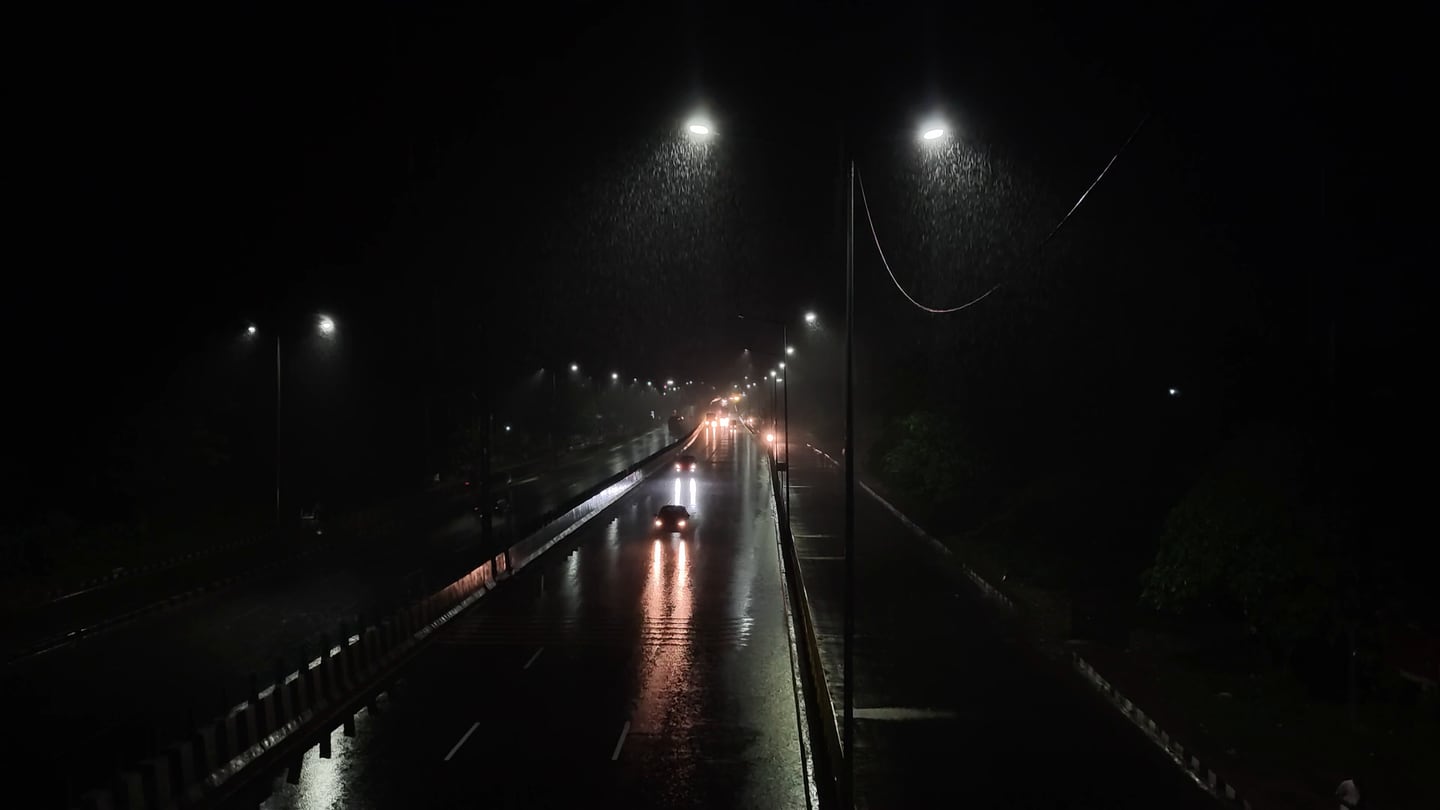 Carretera de noche bajo la lluvia, con autos y las luces reflejadas en el pavimento mojado, vista desde lo alto